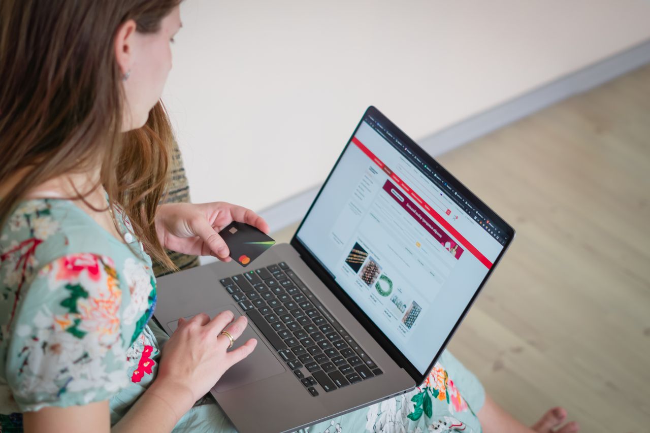about-us Woman in floral dress shopping online with a laptop and credit card indoors.